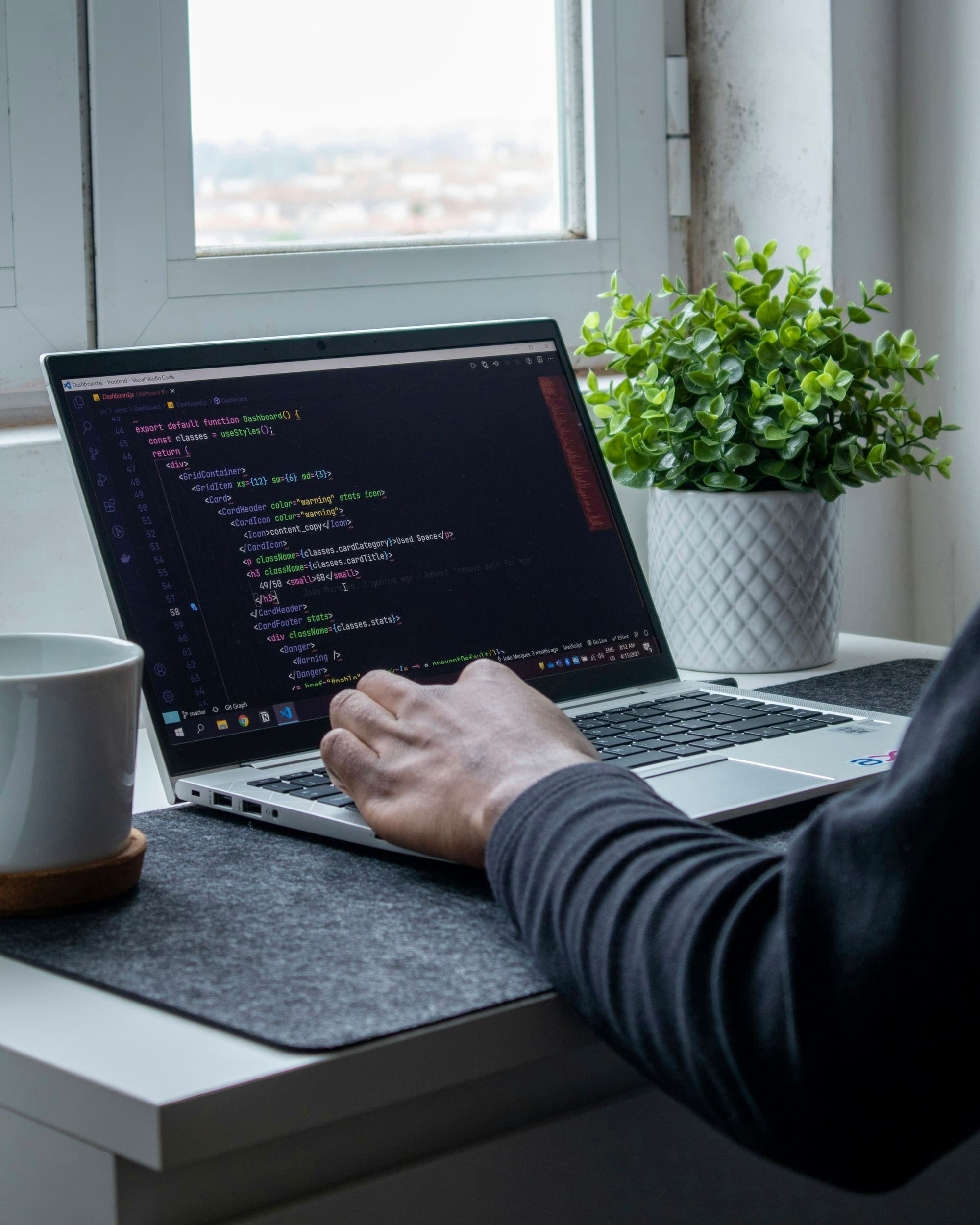 Developer typing code on a laptop beside a plant