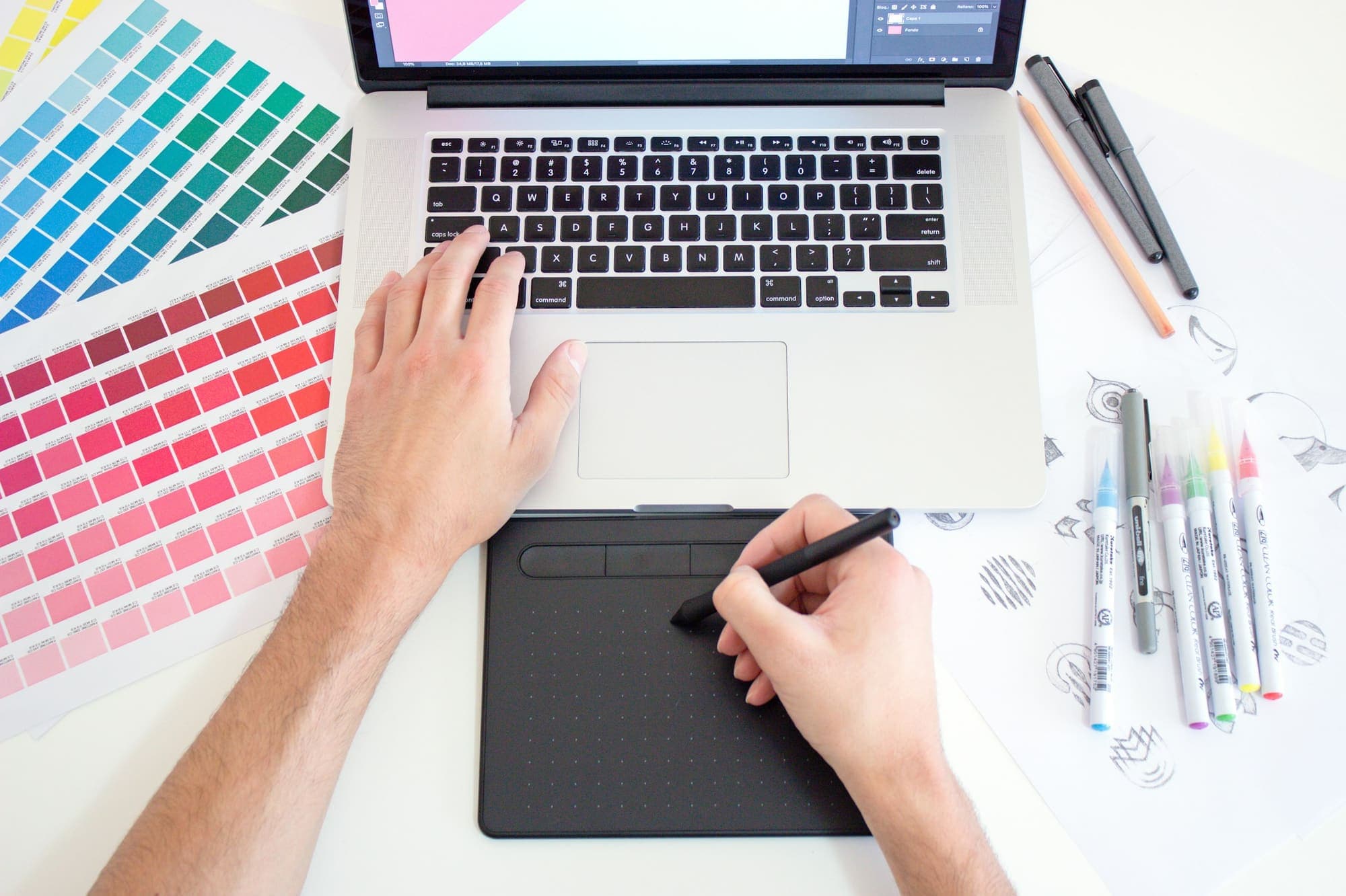 Designer using a drawing tablet with colour swatches and a laptop